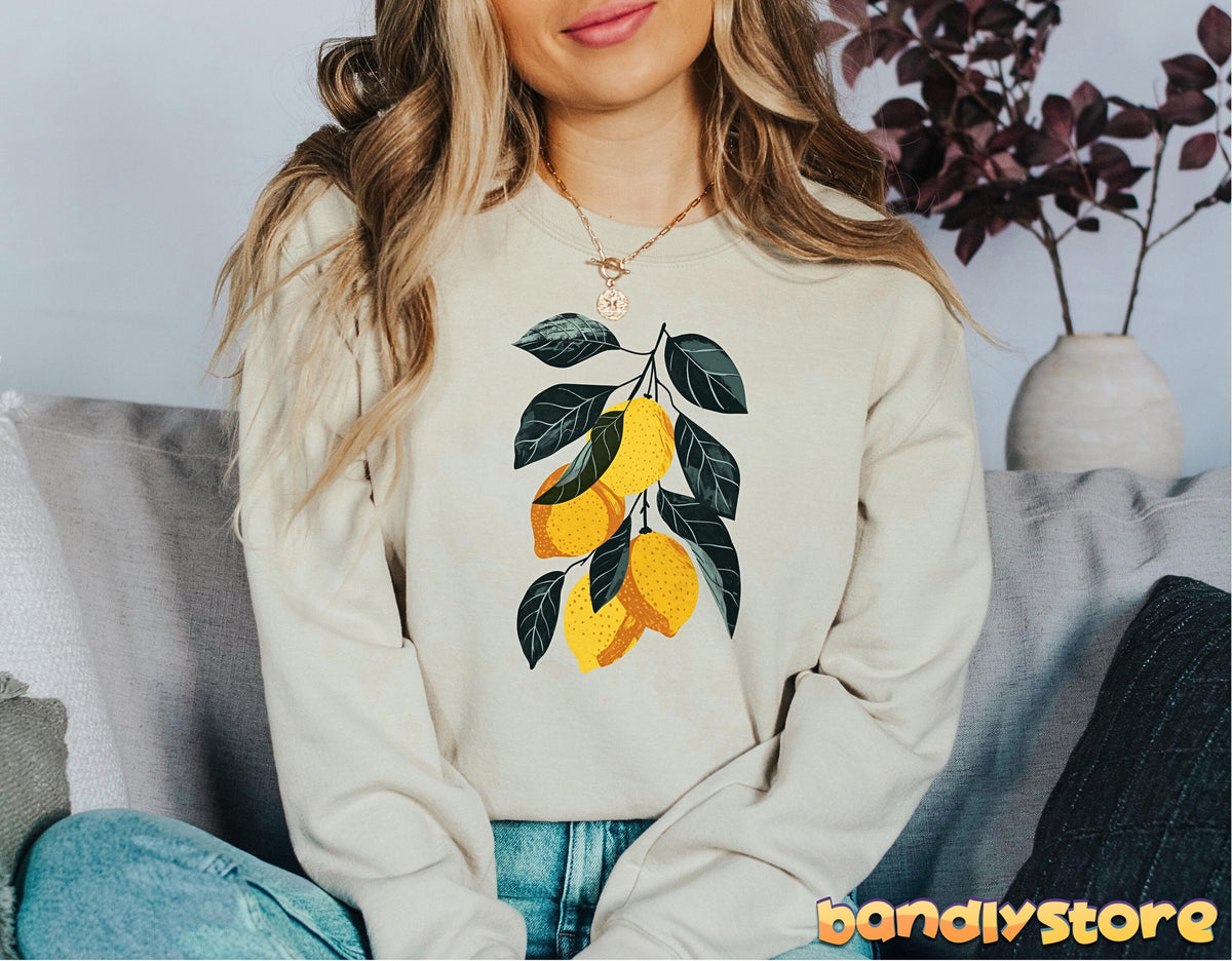 Vintage Lemons Sweatshirt in sand, front view on a seated person on a couch with pillows and a plant vase.