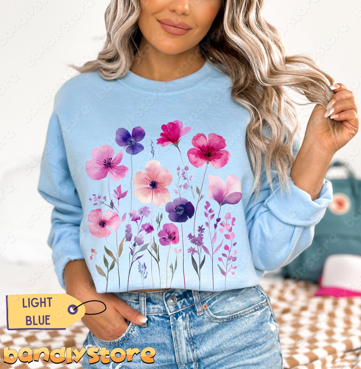 Vintage Wildflowers Sweatshirt in light blue worn by a model facing camera in jeans with a bag in the background.