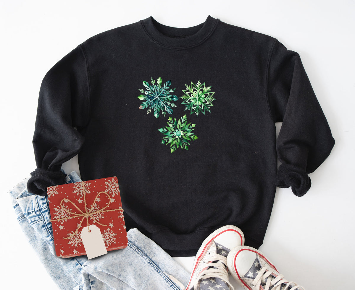 Watercolor Snowflake Sweatshirt in black laid flat on white beside jeans, gift box and sneakers.