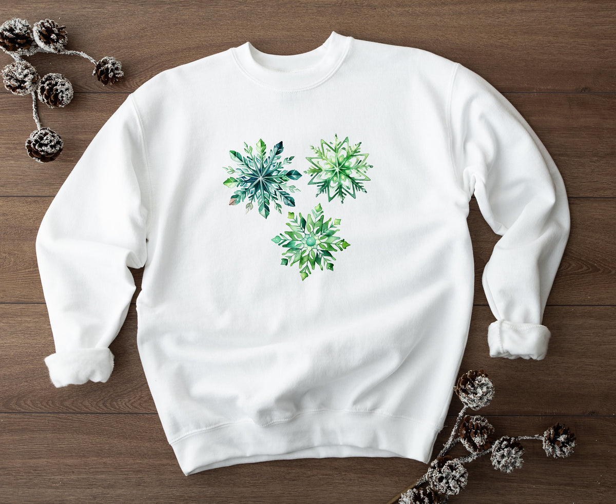 Watercolor Snowflake Sweatshirt in white flat on wood with frosted pinecones nearby.