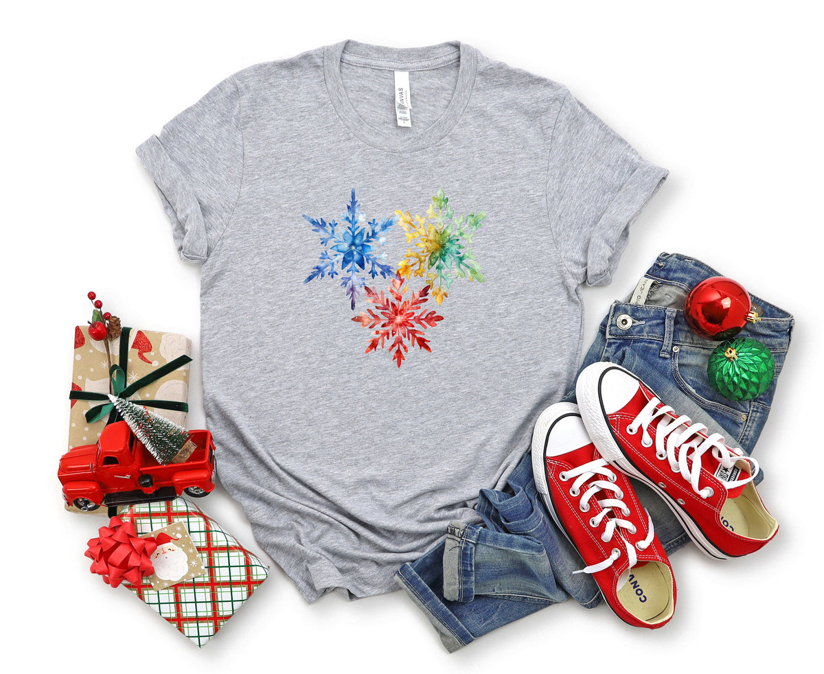 Colorful Watercolor Snowflakes T-Shirt in Athletic Heather laid flat with gifts, red truck, jeans and sneakers.