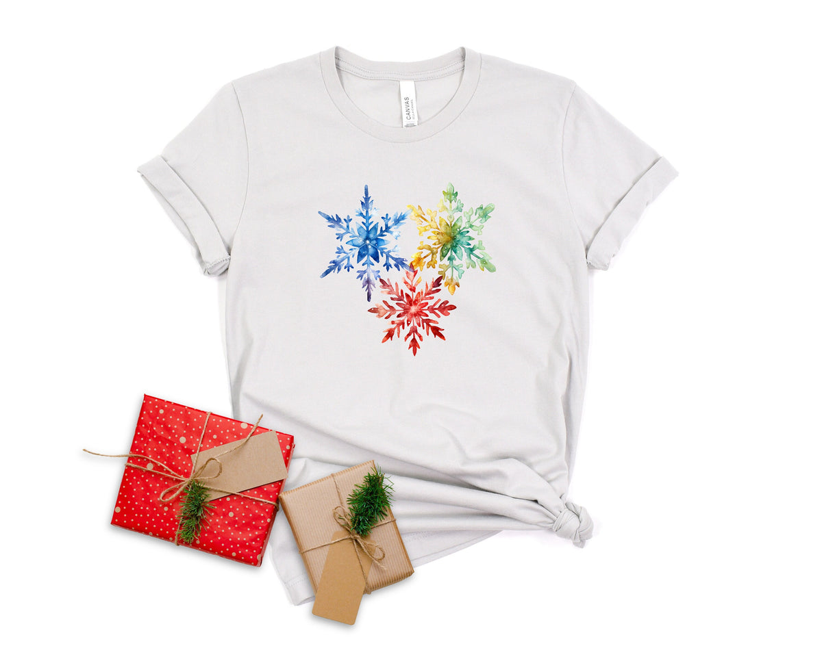 Colorful Watercolor Snowflakes T-Shirt in silver laid flat beside two wrapped gifts.
