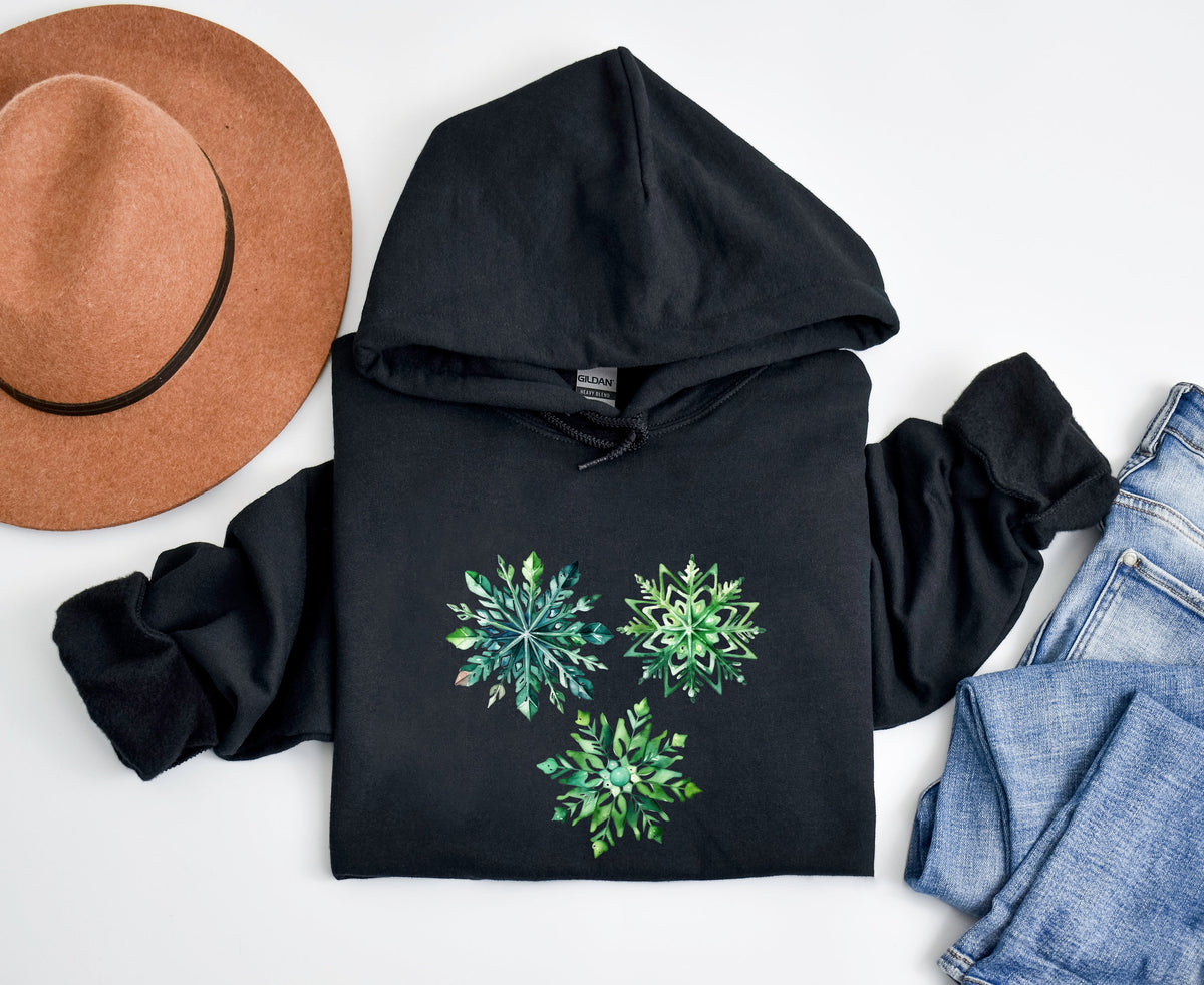 Watercolor Snowflakes Hoodie in black, top-down flat lay beside a brown hat and blue jeans.