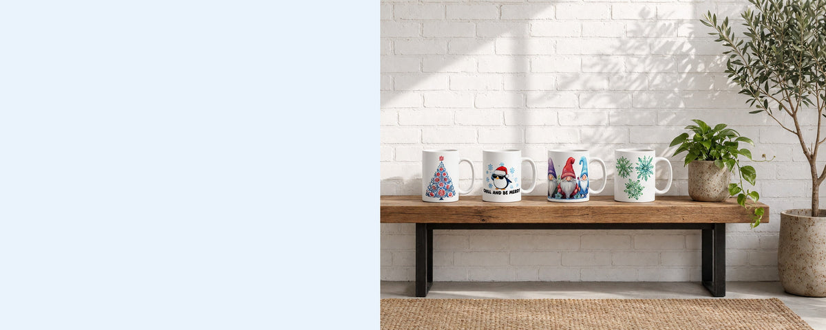 Four printed ceramic coffee mugs in a row on a wooden console table against a sunlit white brick wall, with a pothos plant, an olive branch in a vase and an olive tree