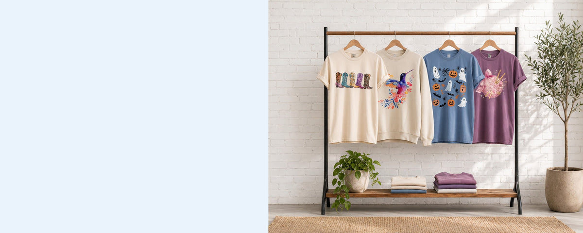 4 printed garments on wooden hangers on a wood and iron clothing rack against a sunlit white brick wall, with an olive tree, trailing pothos and folded tees on the shelf below