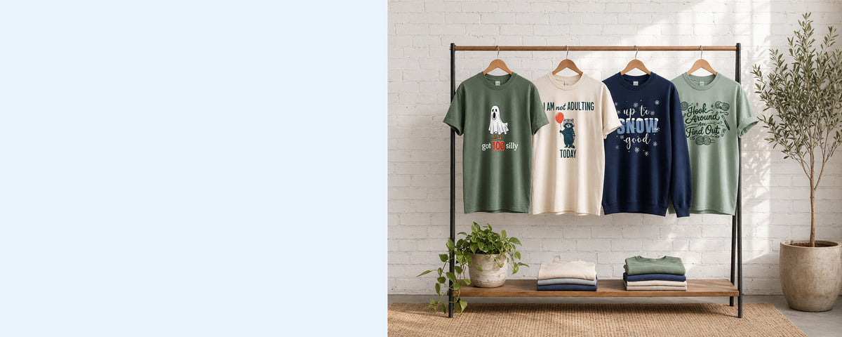 4 printed garments on wooden hangers on a wood and iron clothing rack against a sunlit white brick wall, with an olive tree, trailing pothos and folded tees on the shelf below