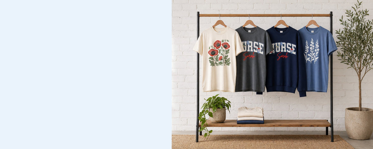 4 printed garments on wooden hangers on a wood and iron clothing rack against a sunlit white brick wall, with an olive tree, trailing pothos and folded tees on the shelf below