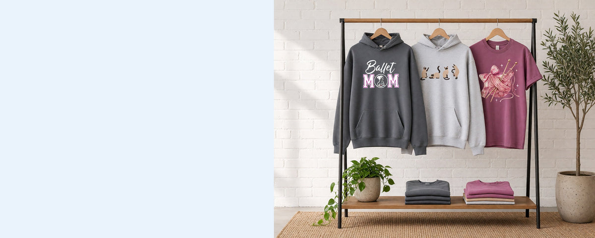 3 printed garments on wooden hangers on a wood and iron clothing rack against a sunlit white brick wall, with an olive tree, trailing pothos and folded tees on the shelf below
