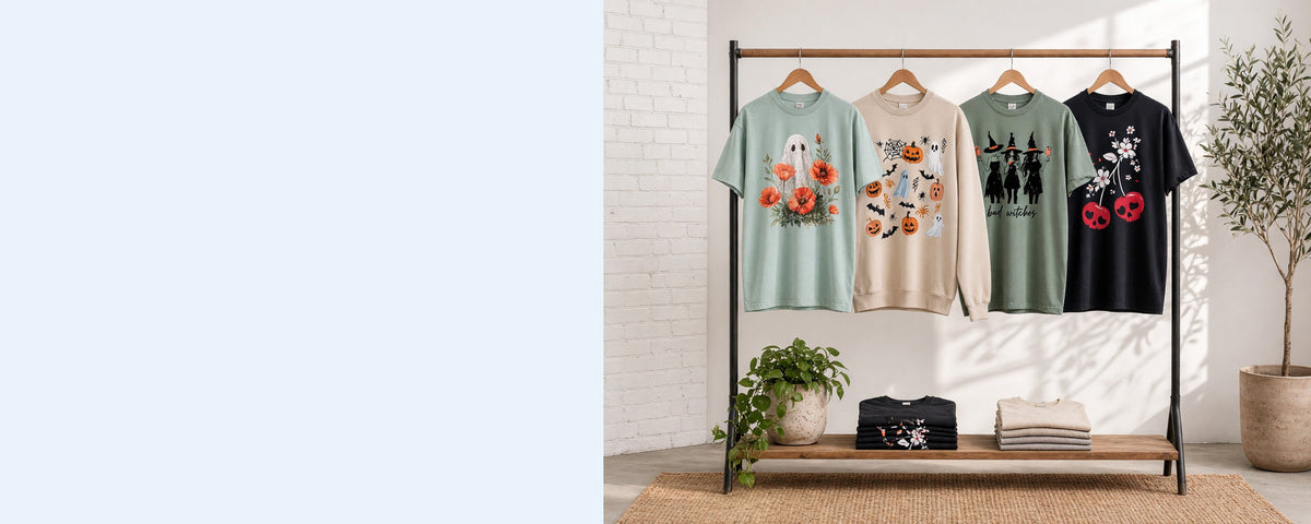 4 printed garments on wooden hangers on a wood and iron clothing rack against a sunlit white brick wall, with an olive tree, trailing pothos and folded tees on the shelf below