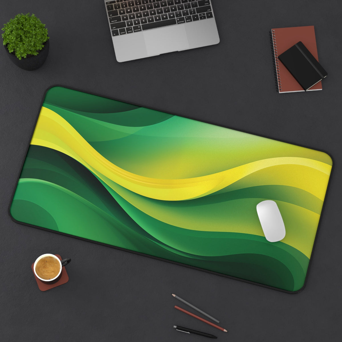 Abstract Desk Mat in green and yellow waves on a dark desk with laptop, mouse, coffee and pencils, 16 × 32 inches.