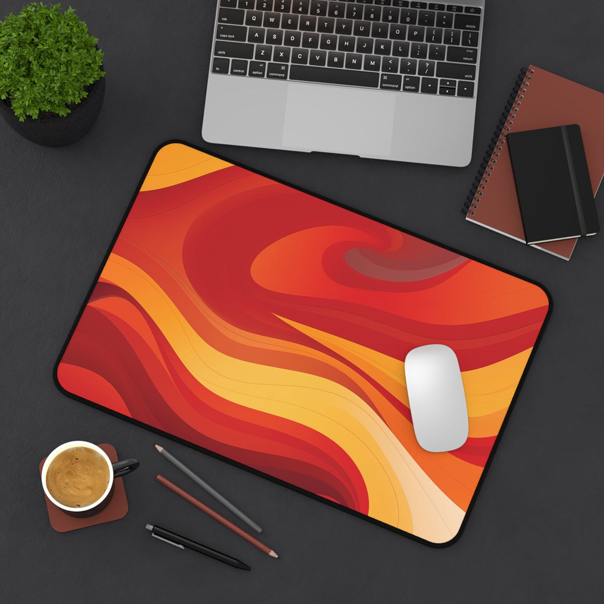 Abstract Lava Desk Mat in red-orange waves on a dark desk with laptop, plant, coffee, pens and notebooks, 12 × 18 inches