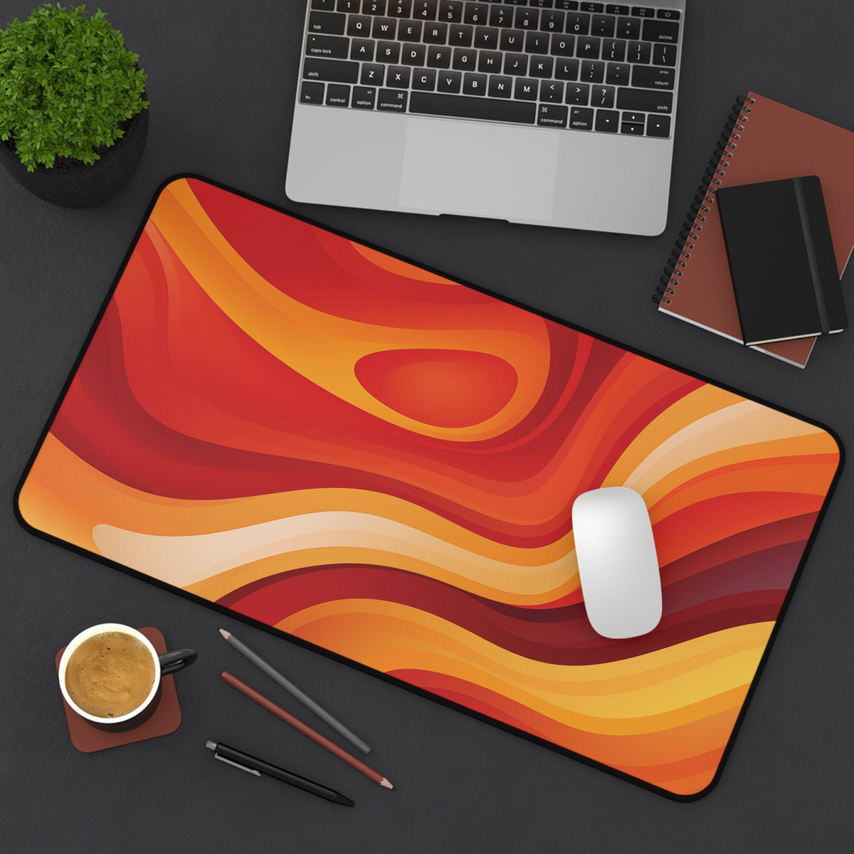 Abstract Lava Desk Mat in warm red-orange waves on a dark desk with laptop, mouse, coffee and pens, 12 × 22 inches.