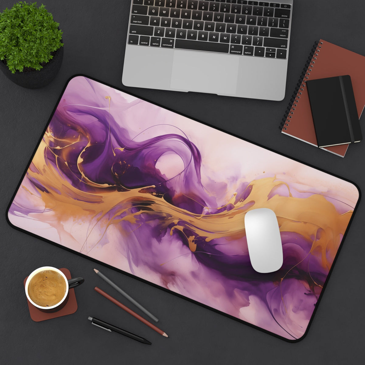 Abstract Purple And Gold Desk Mat on a dark desk with laptop, plant, coffee, pens and notebooks, 12 × 22 inches.