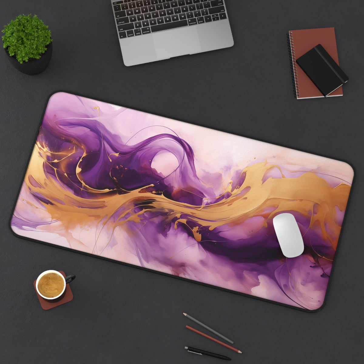 Abstract Purple And Gold Desk Mat on a dark desk with laptop, plant, coffee, notebooks, pens, and mouse, 16 × 32 inches.
