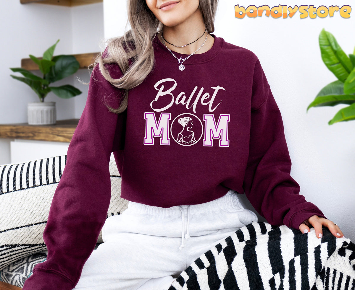 Ballet Mom Sweatshirt in maroon on a woman sitting indoors beside plants and striped cushions.