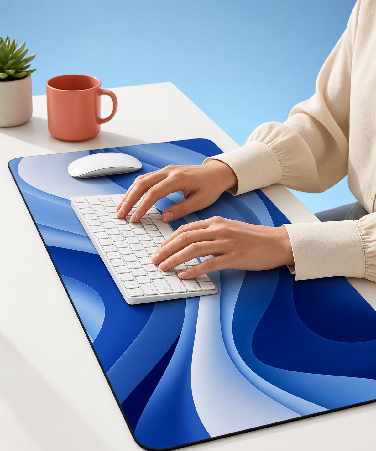 Hands typing on a white keyboard on a printed desk mat, with a coral mug and a plant, against a sky-blue backdrop