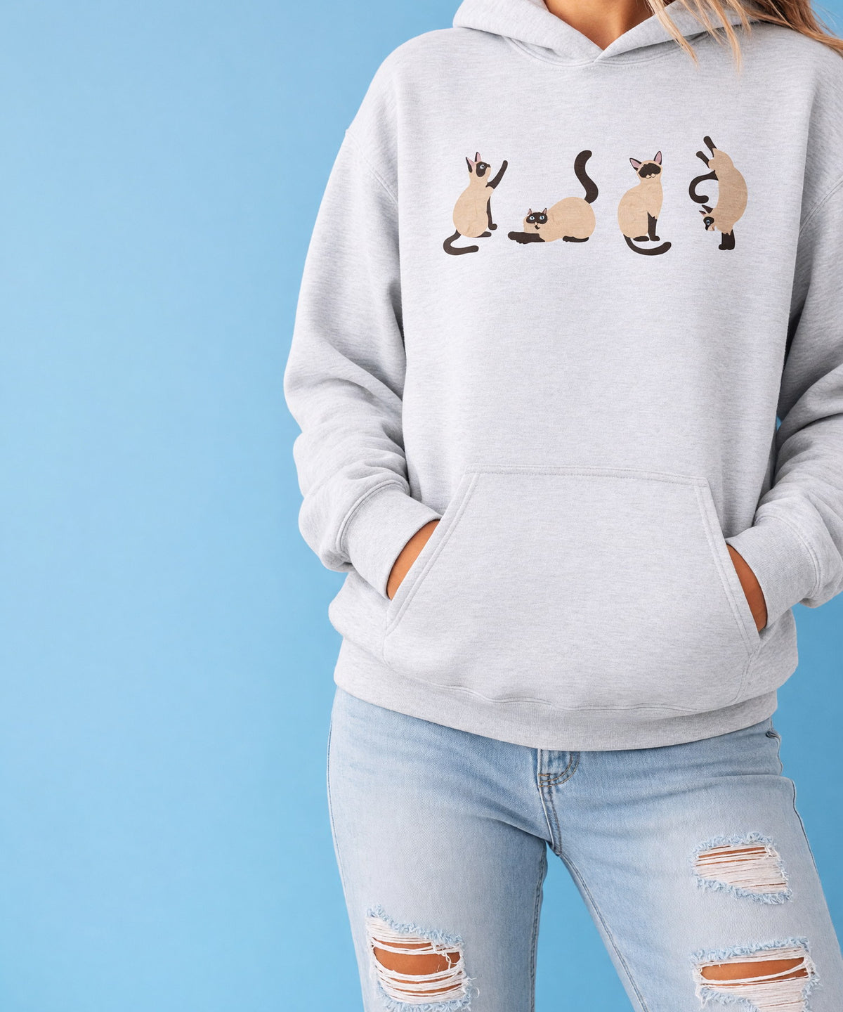 A woman in a printed pullover hoodie with her hands in the front pocket, cropped at the chest, against a sky-blue backdrop