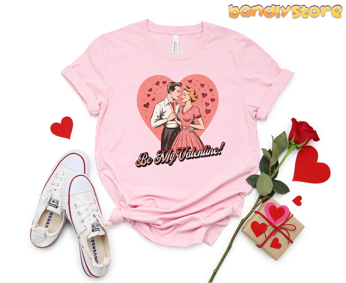 Be Mine Valentine T-Shirt in pink top-down flat lay next to sneakers, rose, gift box and hearts.