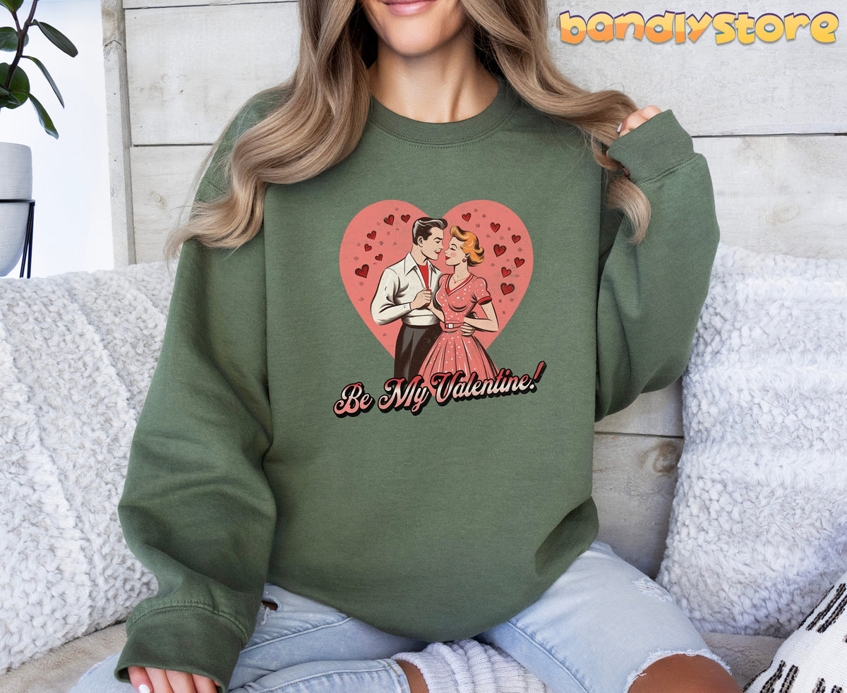 Be Mine Valentine Sweatshirt in military green on a seated person against a wood wall with white pillows and a plant.