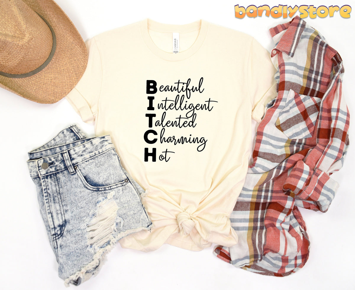 Bitch Definition T-Shirt in natural, top-down flat lay with straw hat, shorts and plaid shirt.