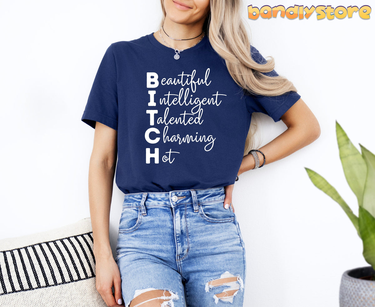 Bitch Definition T-Shirt in navy on a woman standing by a white wall beside a plant and striped cushion.