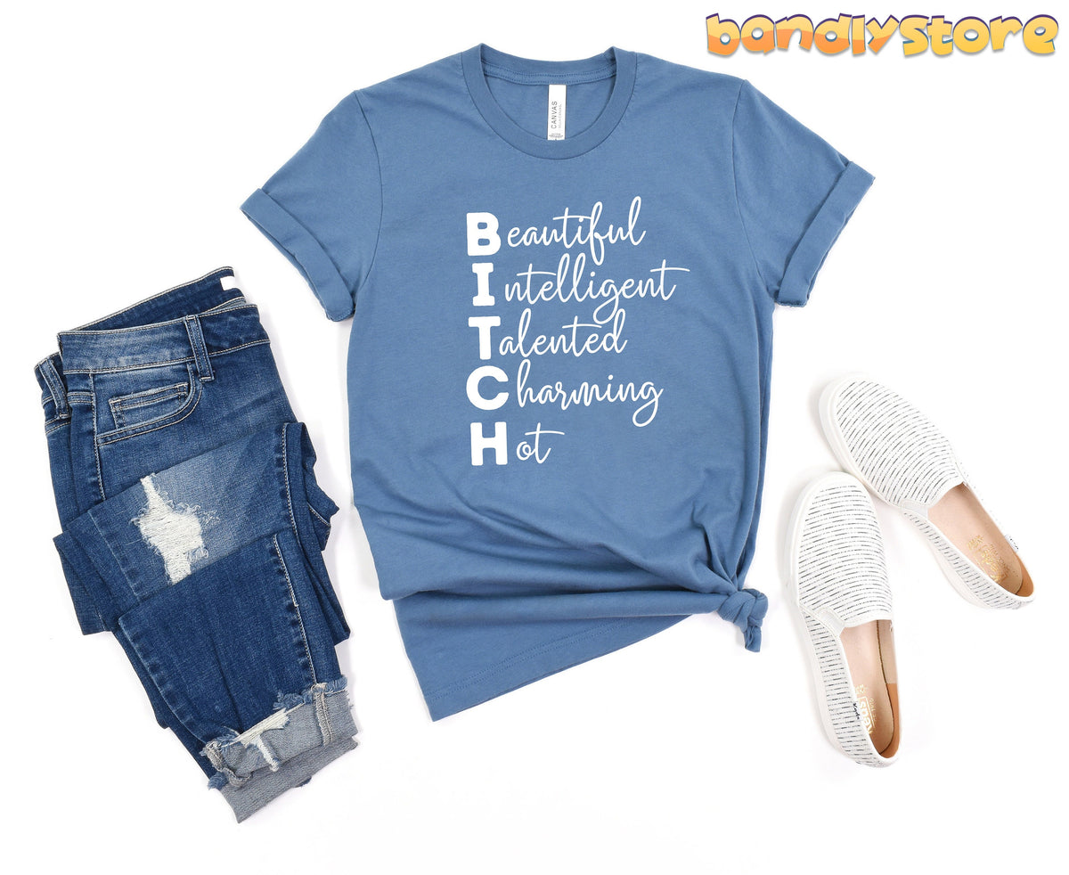 Bitch Definition T-Shirt in steel blue flat-laid beside ripped jeans and white slip-ons.