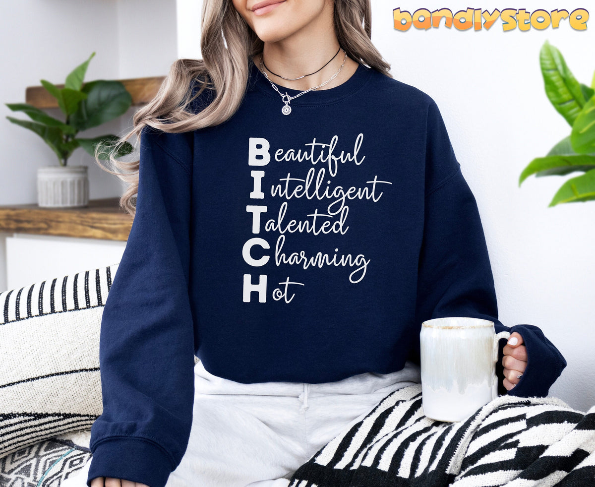 Bitch Definition Sweatshirt in navy on a seated woman holding a mug amid plants and striped textiles.