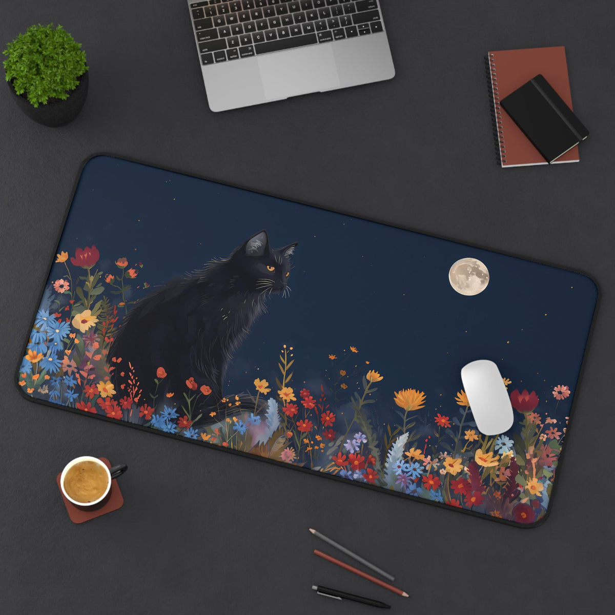 Black Cat And The Moon Desk Mat 16 × 32 inches from above on a dark desk with laptop, plant, notebooks, coffee and pencils.