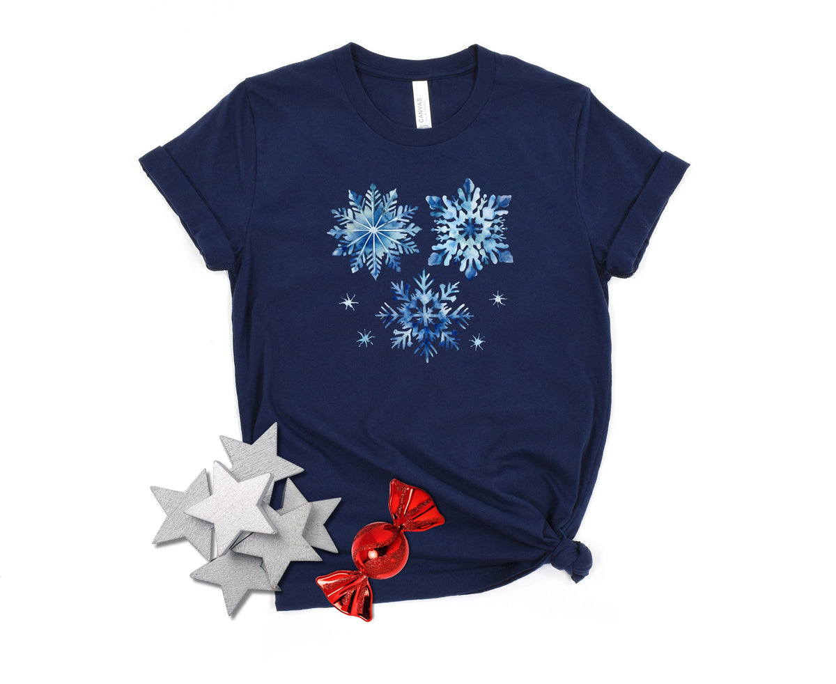 Watercolor Snowflakes T-Shirt in navy on white, overhead flat lay with silver stars and red candies.