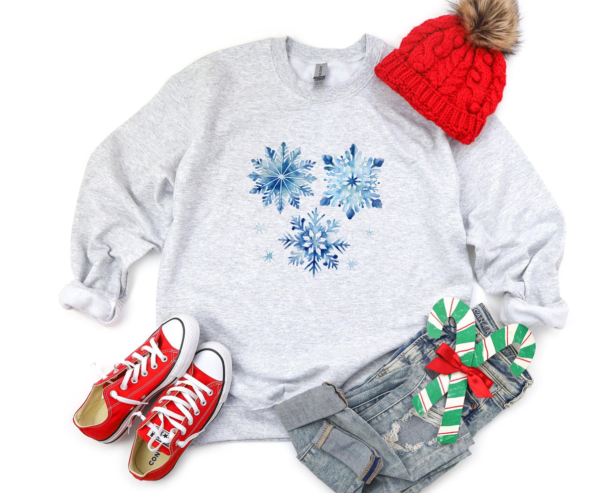 Blue Watercolor Snowflakes Sweatshirt in ash, flat lay with red beanie, sneakers, jeans and candy canes.