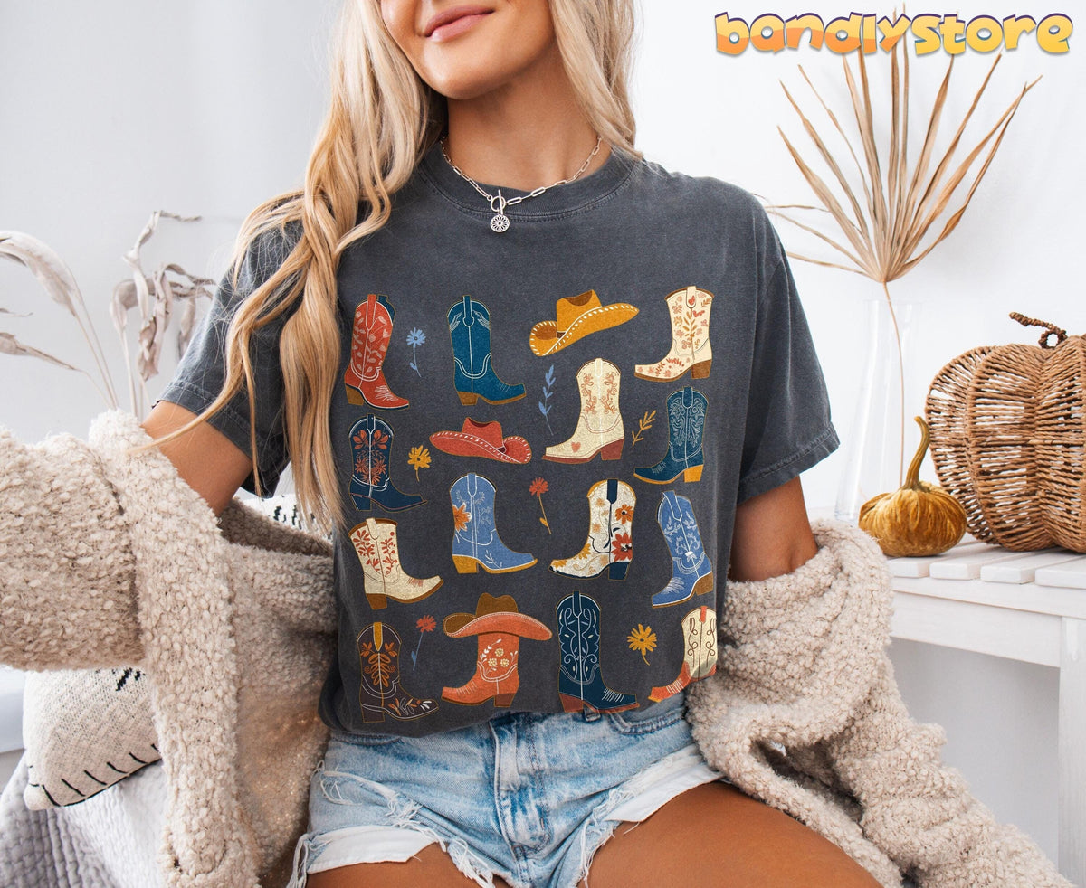 Boho Cowgirl Boots T-Shirt in Pepper on seated model, front view, beside dried plants, pumpkin and wicker basket.