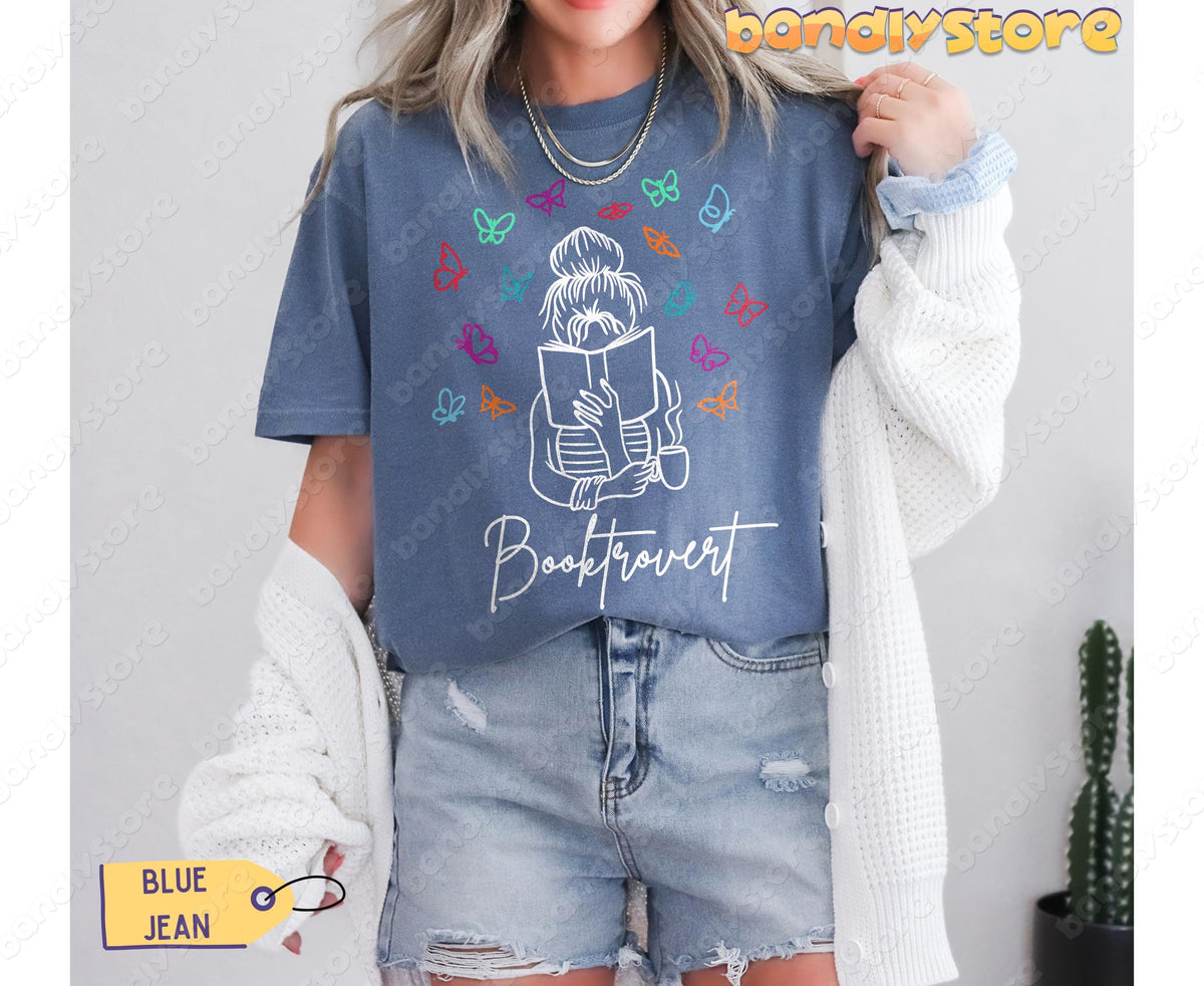 Booktrovert T-Shirt in Blue Jean on a model holding a cardigan beside a cactus, front view.