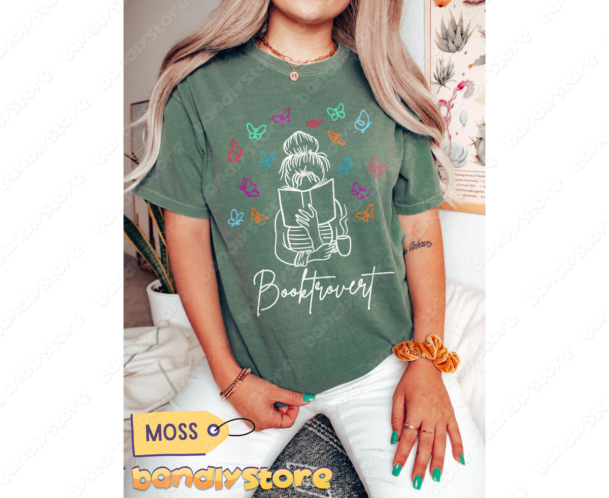 Booktrovert T-Shirt in moss, modeled front-on indoors with plants and a botanical print nearby.