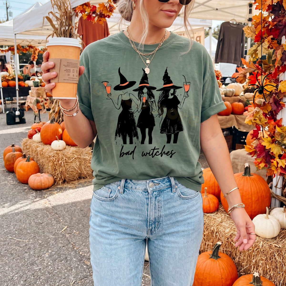 Boujee Bad Witches T-Shirt in moss, front view on a woman amid pumpkins and hay at a fall market.
