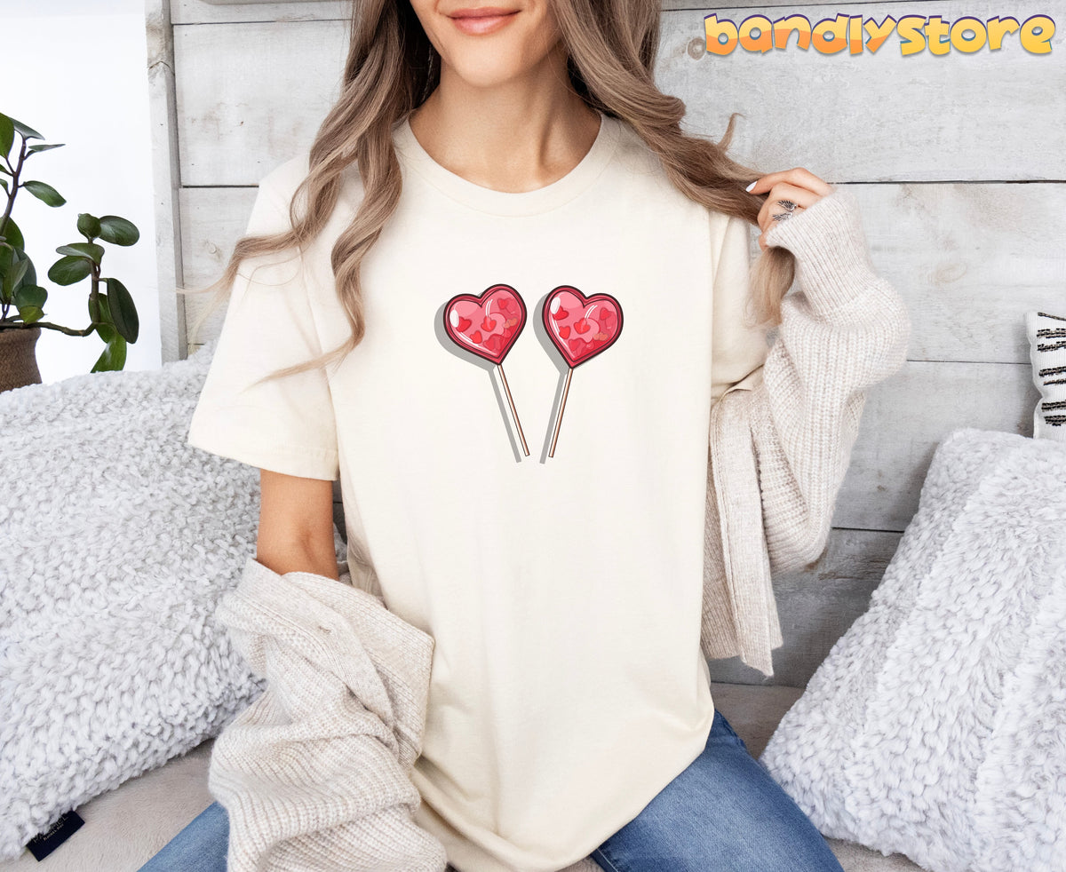 Cute Candy Hearts T-Shirt in Natural, worn front-facing by a seated model amid pillows, a plant and wood wall.