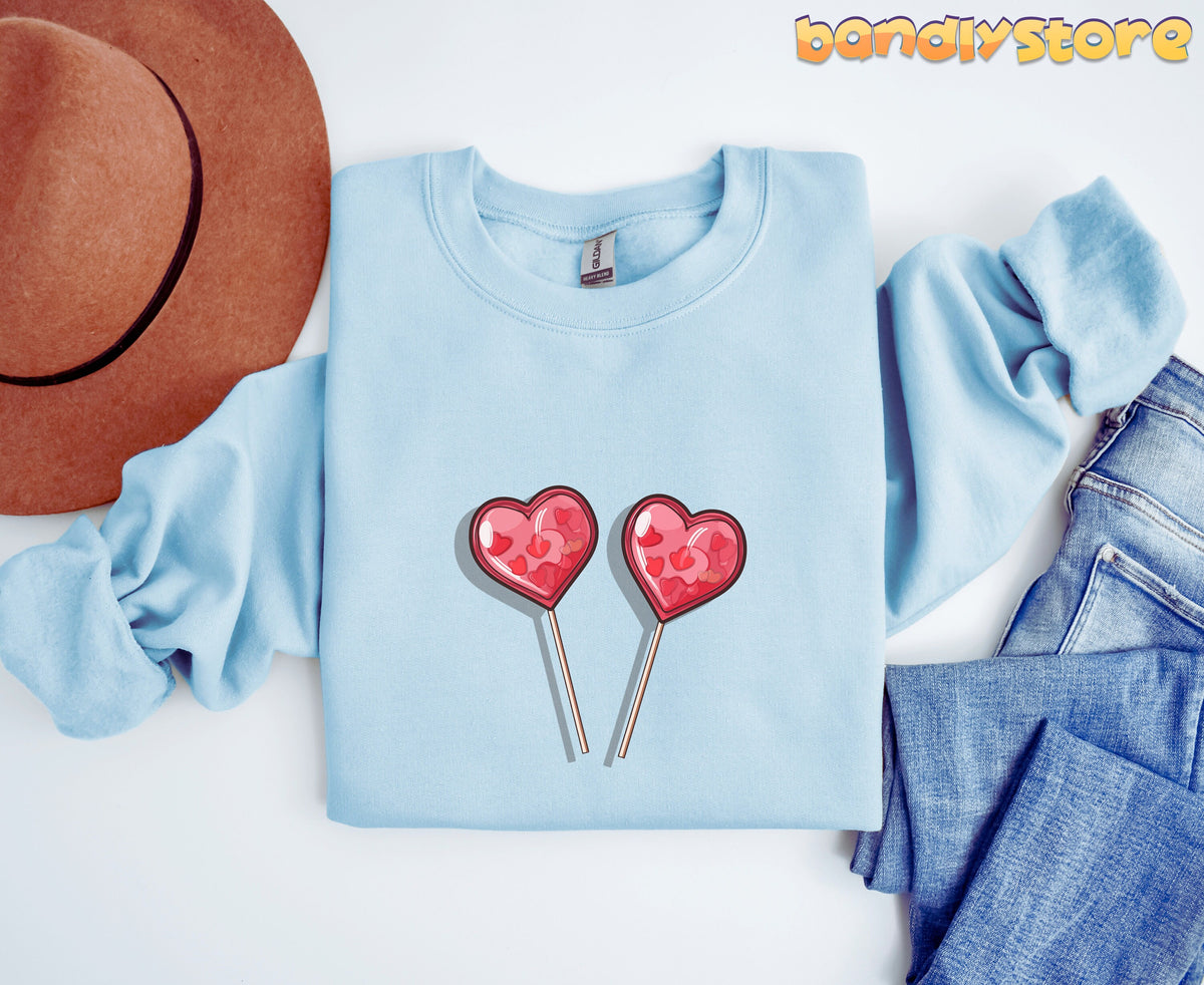 Cute Candy Hearts Sweatshirt in light blue, flat-laid overhead beside a brown hat and jeans.
