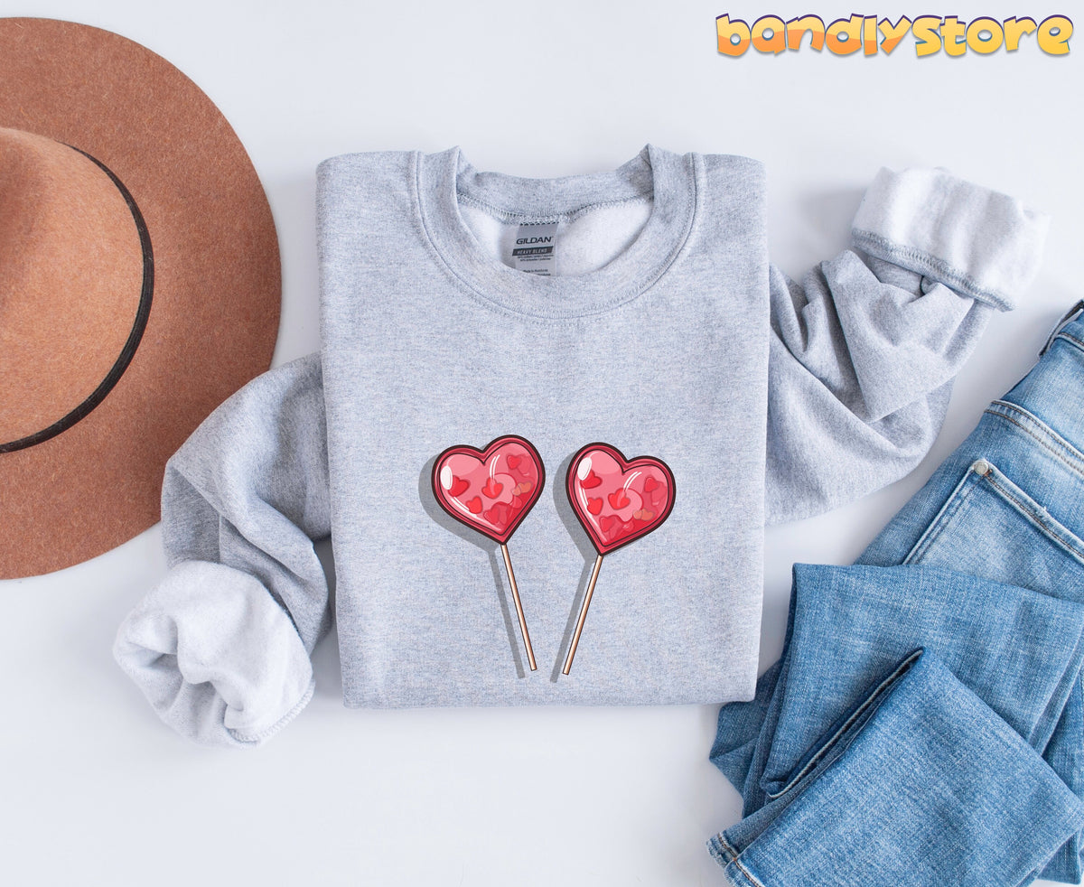 Cute Candy Hearts Sweatshirt in Sport Grey folded flat from above beside a brown hat and blue jeans on white.
