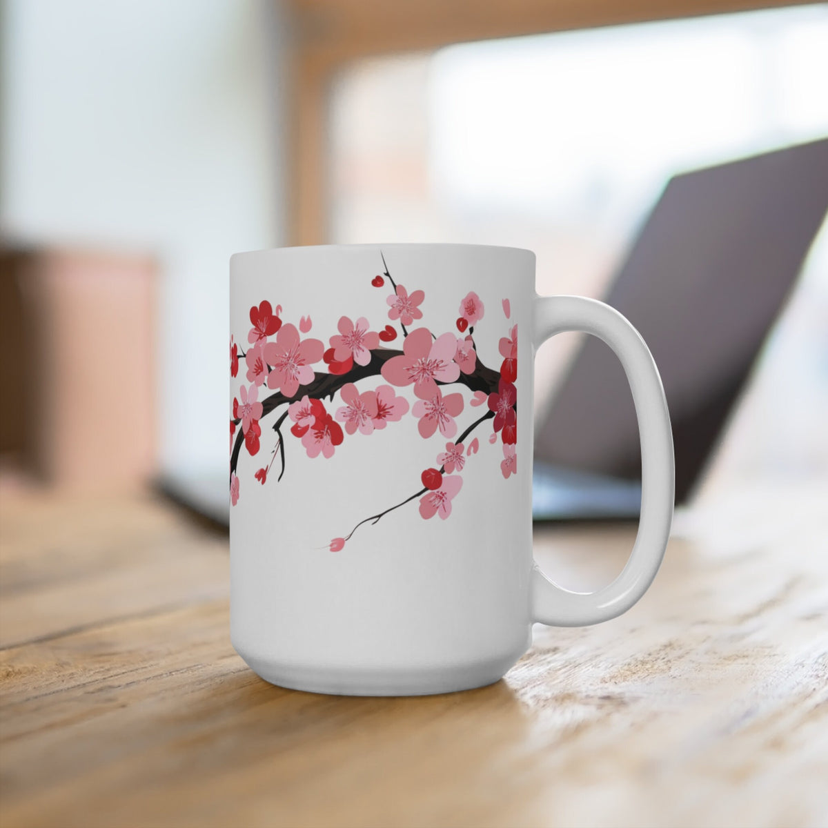 Cherry Blossom Mug on a wooden table with a blurred laptop behind, angled to show the right-side handle.