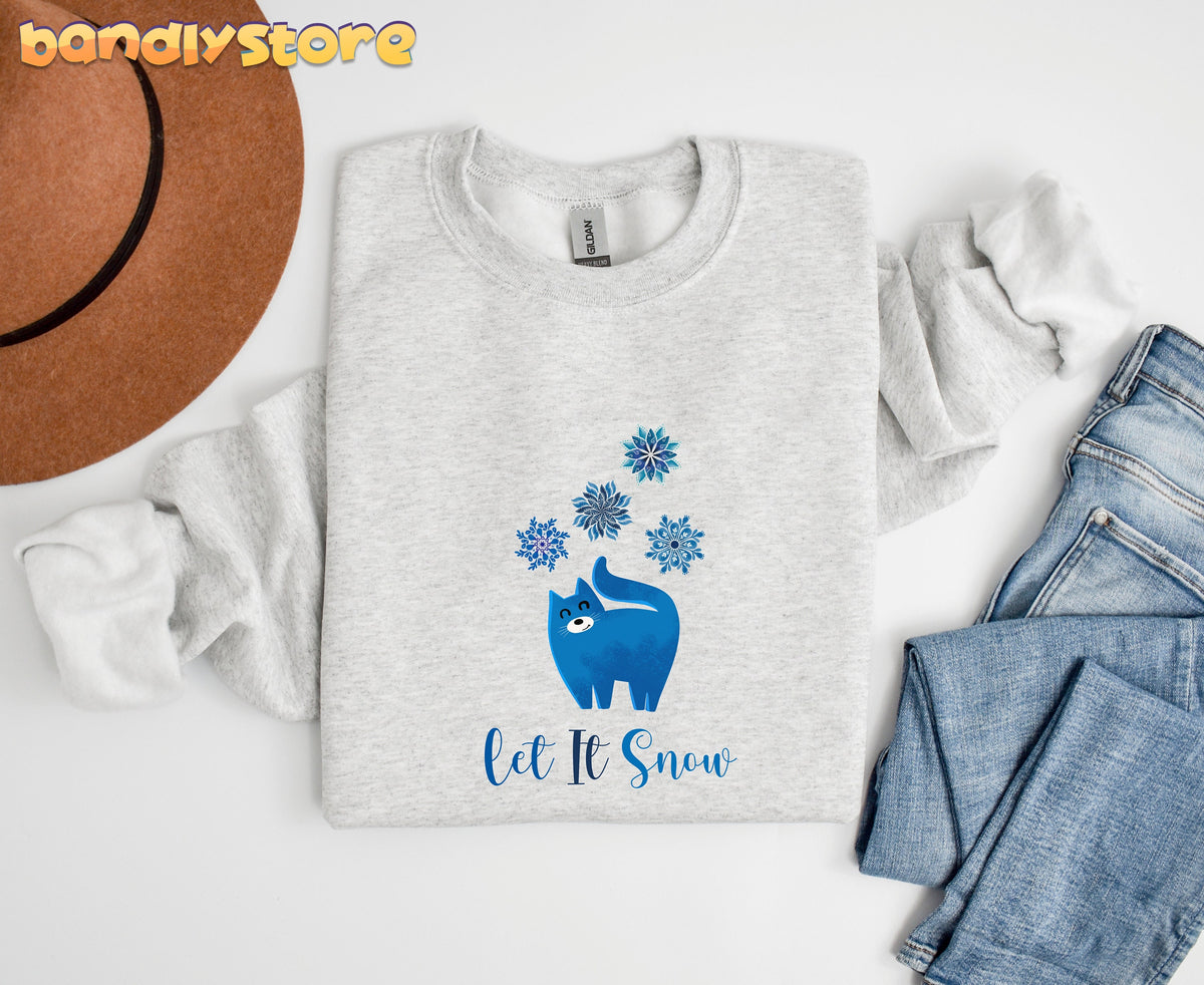 Christmas Cat Let It Snow Sweatshirt in ash folded flat beside a brown hat and blue jeans on white.