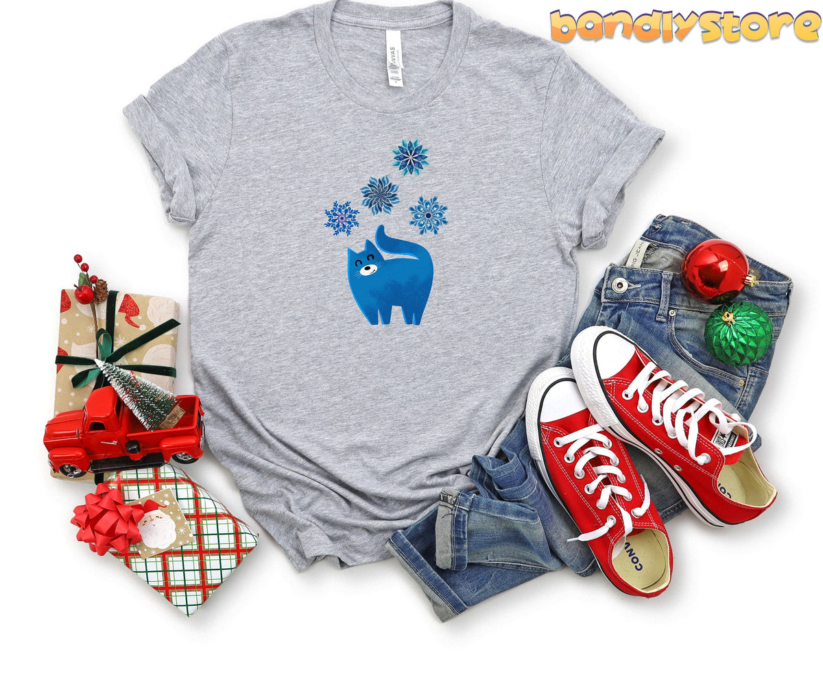 Christmas Cat and Snowflakes T-Shirt in Athletic Heather flat-laid with gifts, jeans, red sneakers and ornaments.