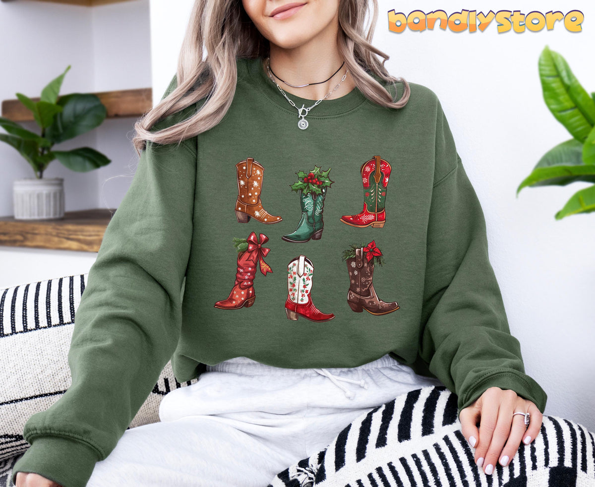 Christmas Cowgirl Boots Sweatshirt in military green, worn seated indoors among plants and pillows with six festive boot graphics.