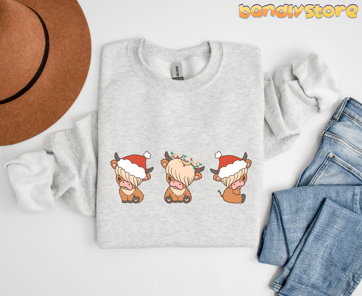 Christmas Highland Cow Trio Sweatshirt in ash, flat-lay with hat left and jeans right of three festive cows.