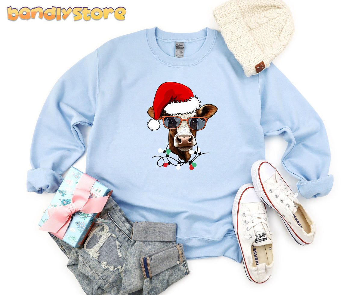 Christmas Cow Sweatshirt in light blue laid flat beside a beanie, sneakers, jeans and wrapped gift.