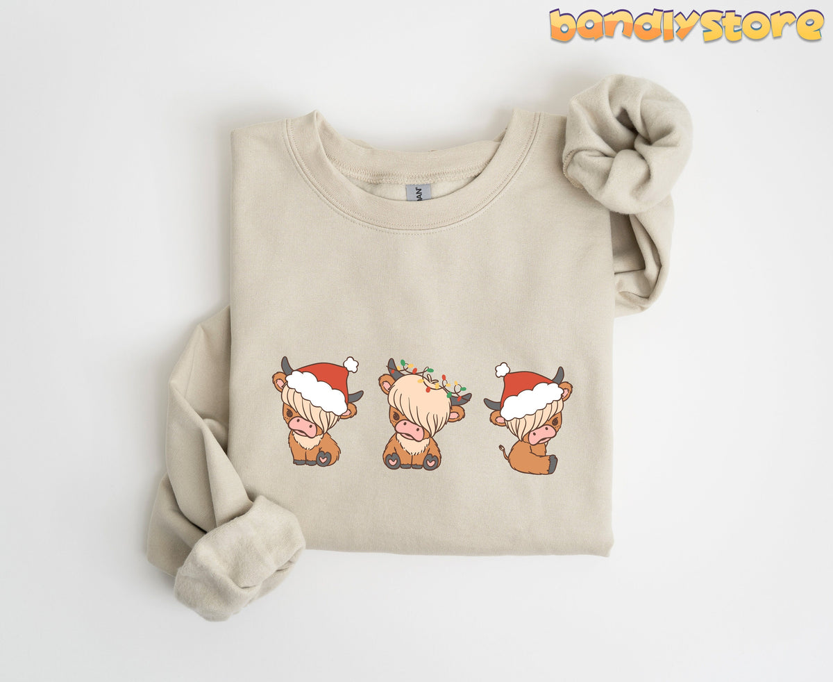Christmas Highland Cow Trio Sweatshirt in sand folded flat on a plain white background.