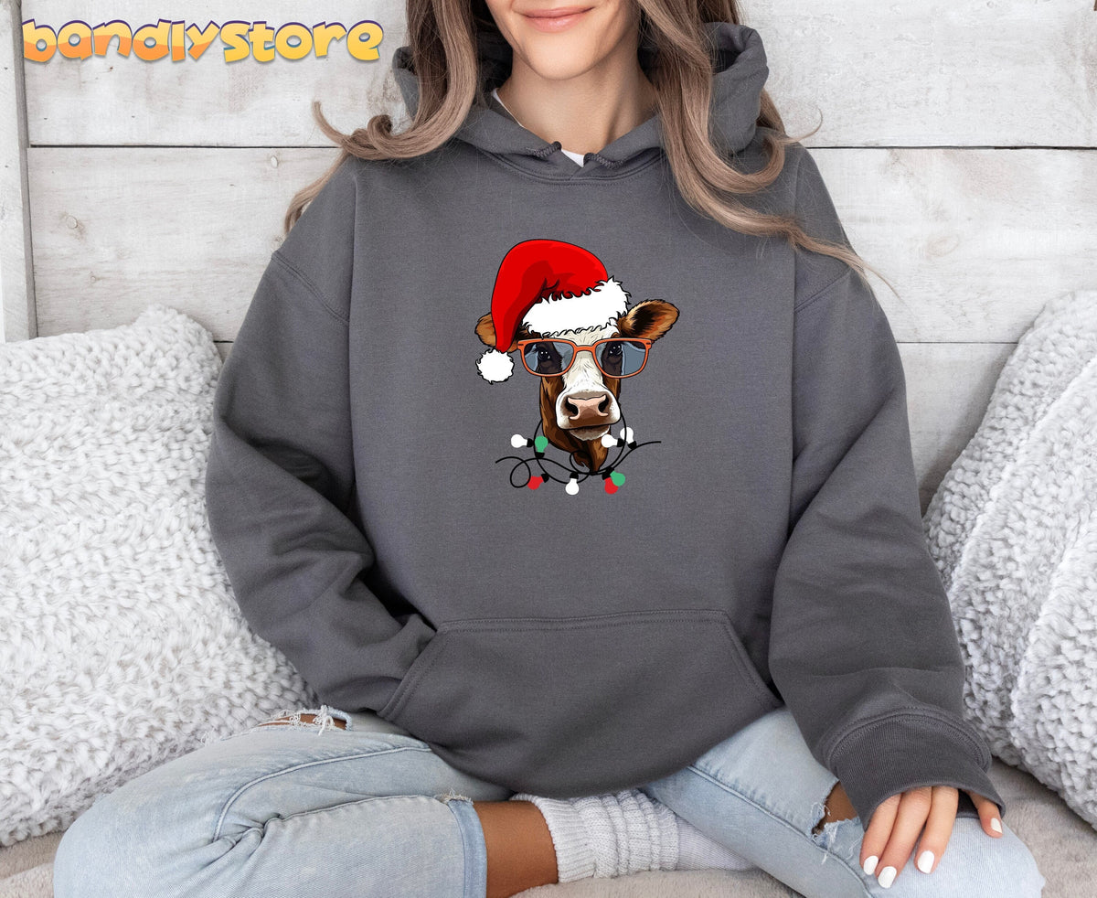 Christmas Highland Cow Hoodie in Sport Grey front-facing on seated person amid white fluffy pillows against wood wall.