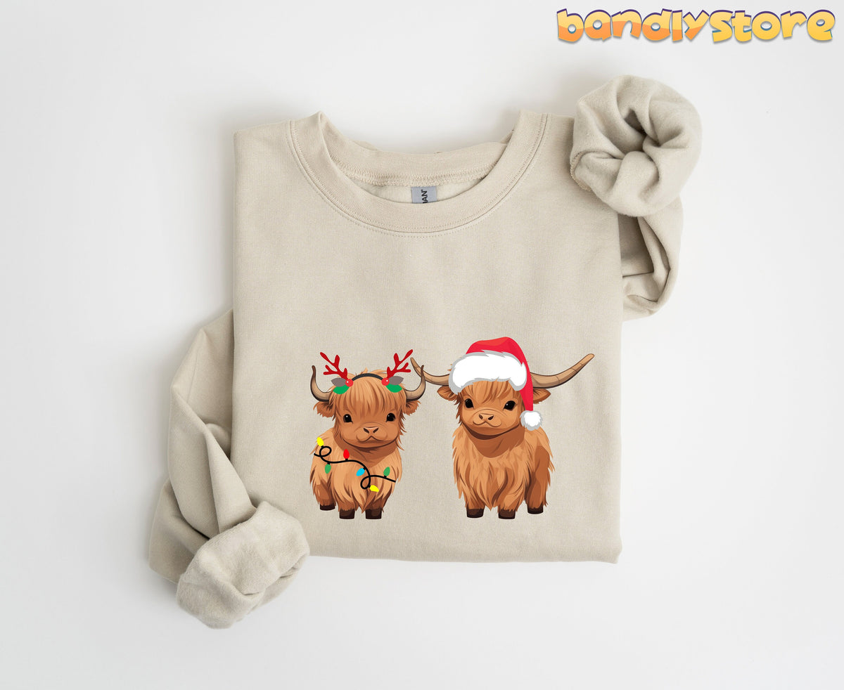 Christmas Highland Cow Sweatshirt in sand, folded flat on white with two festive highland cows on the chest.