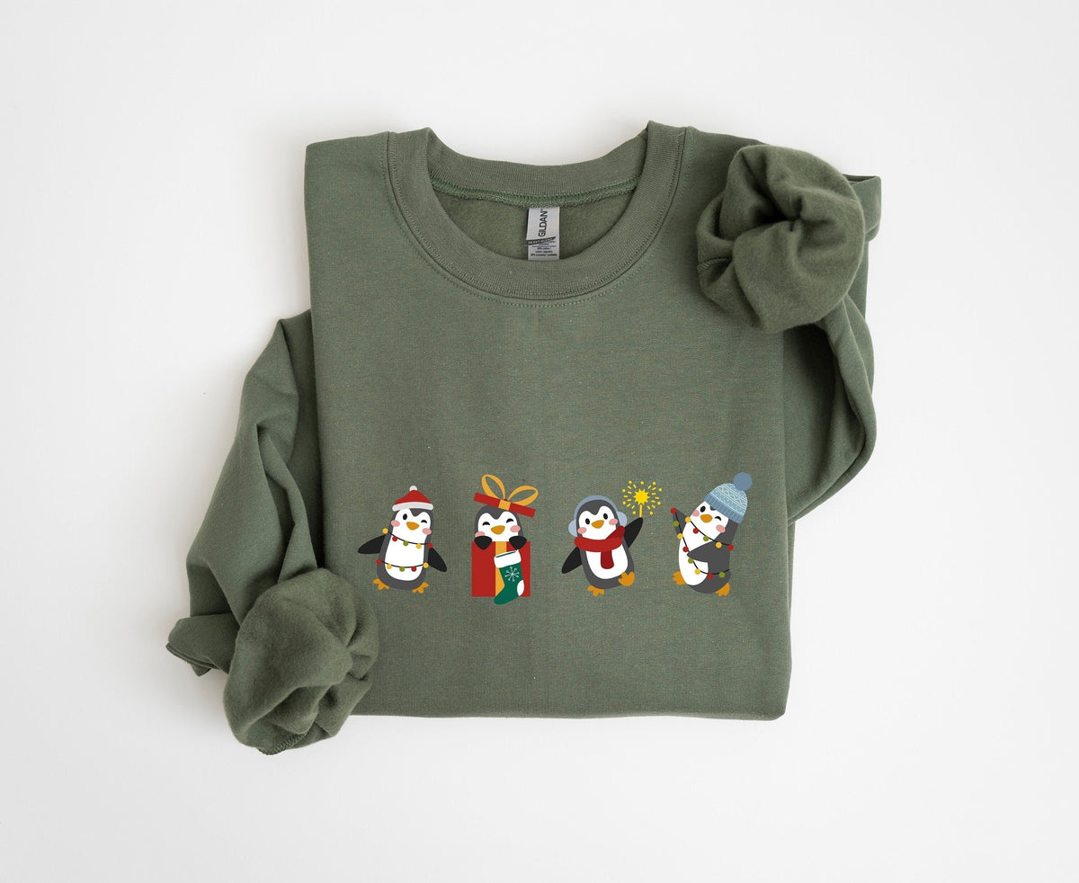 Christmas Penguin Sweatshirt on a Military Green crewneck laid flat, four festive penguins across the chest.