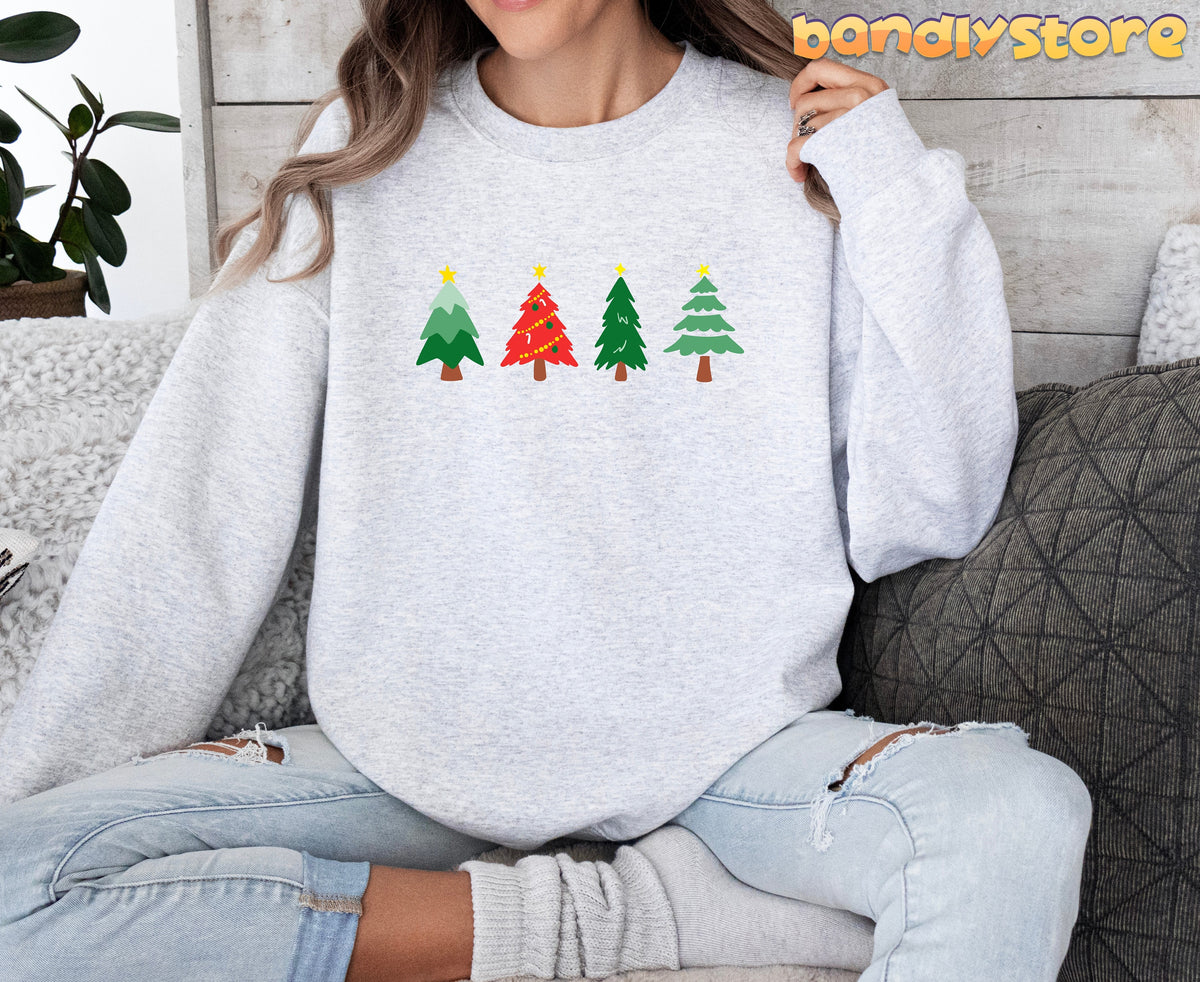 Oh Christmas Tree Sweatshirt in ash on a seated person amid couch pillows, plant and wood wall.