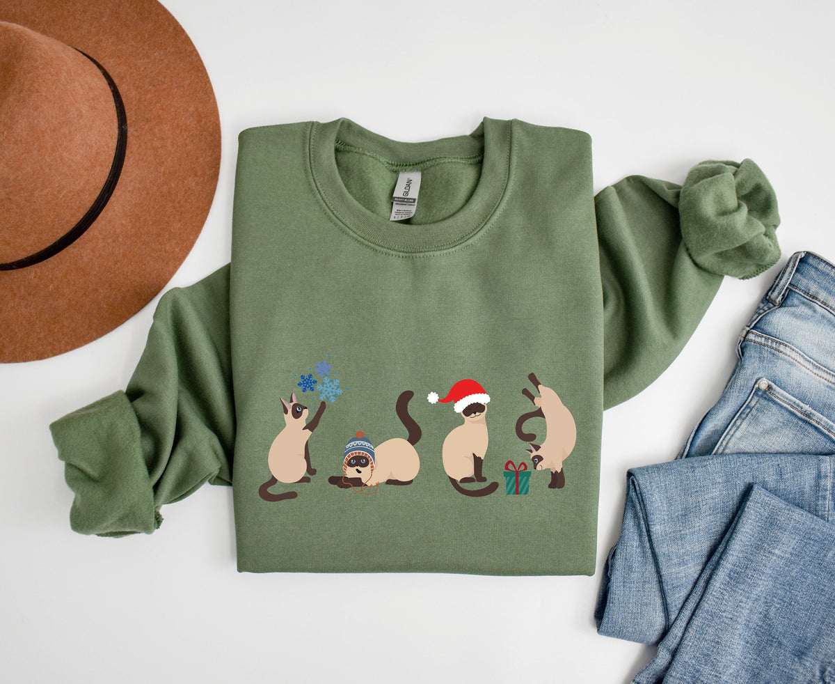 Christmas Siamese Cat Sweatshirt in military green folded flat beside a brown hat and blue jeans.