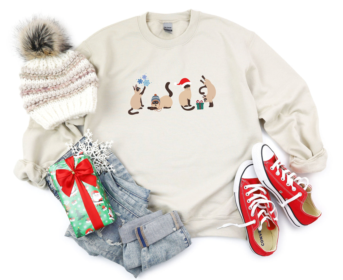 Christmas Siamese Cat Sweatshirt in sand, flat-lay with beanie, gift, jeans and red sneakers beside the printed cats.